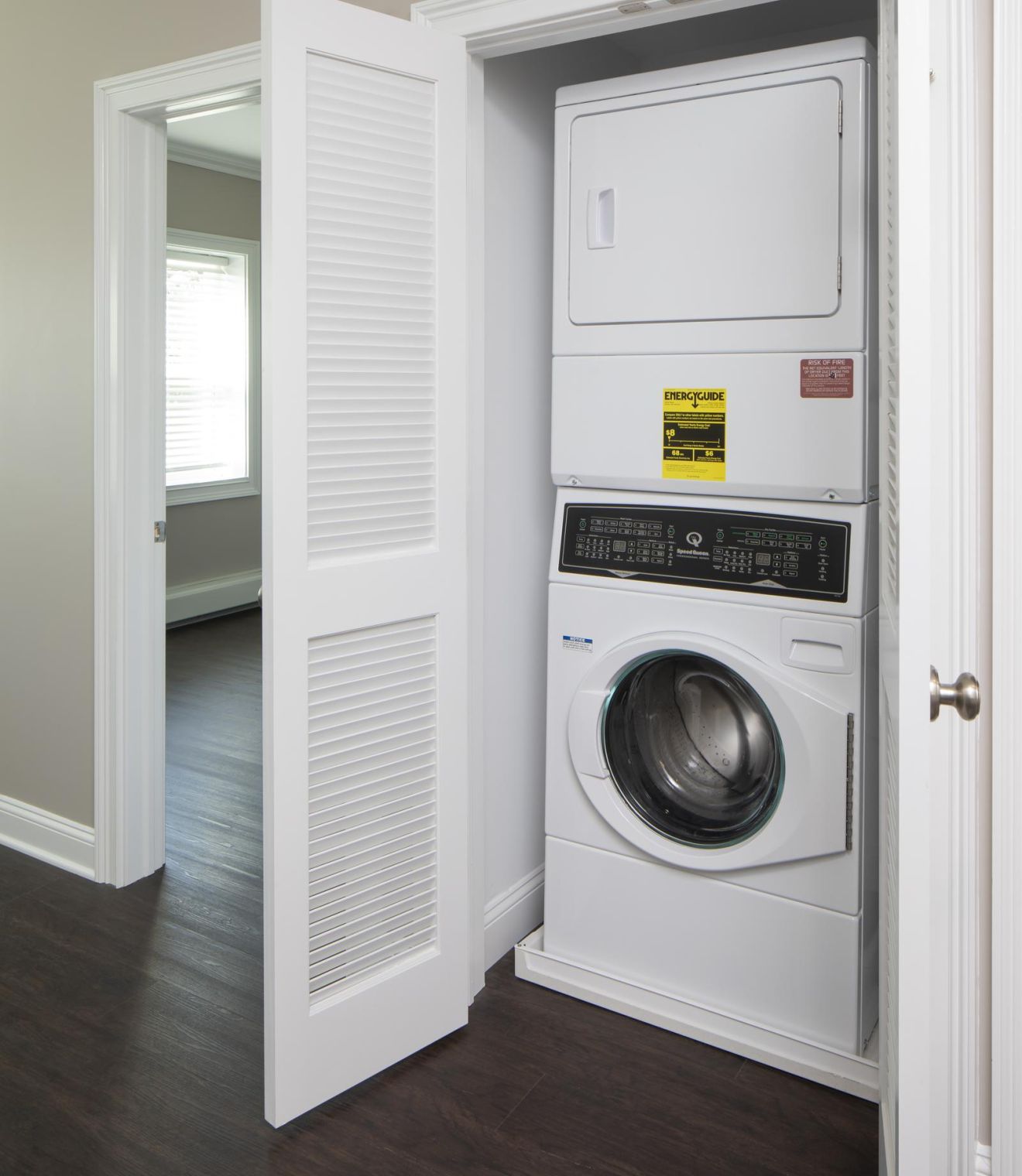 Stacked washer and dryer in a small laundry closet with white folding doors and dark wood floor.