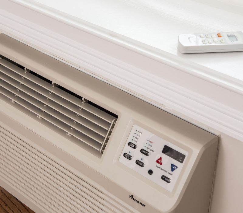 Window air conditioner with control panel and remote placed on a white windowsill above the unit.
