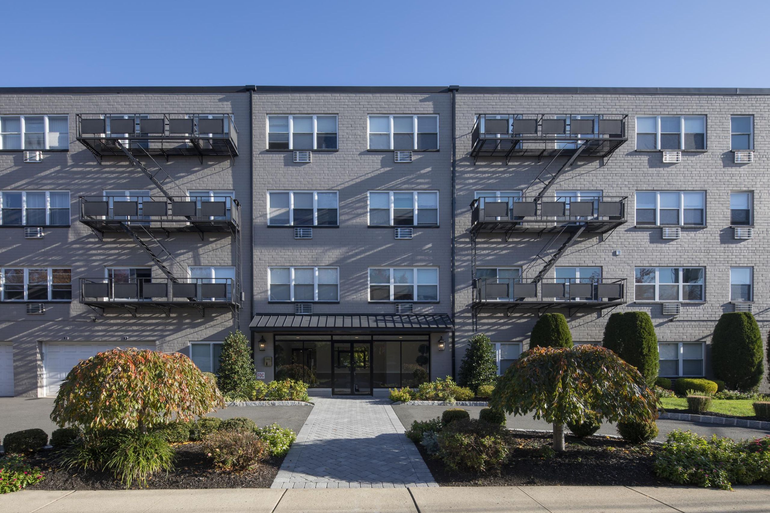 The Cornerstone A modern apartment building with landscaped gardens and a wooden entrance canopy under a partly cloudy sky.