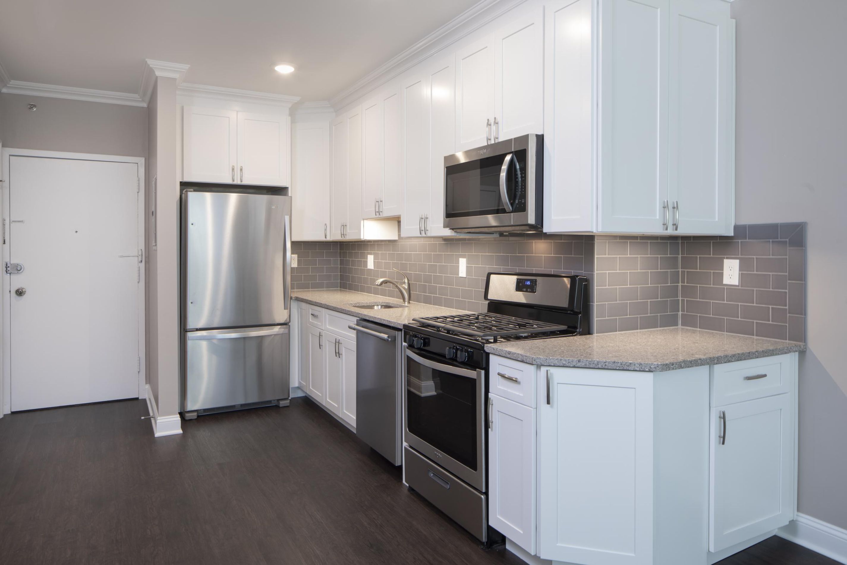 Modern kitchen with white cabinets, stainless steel appliances, and gray tile backsplash.