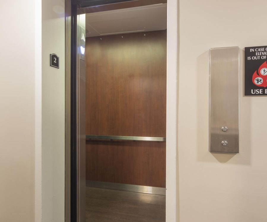 An open elevator with wood-paneled walls on the second floor in a building hallway.