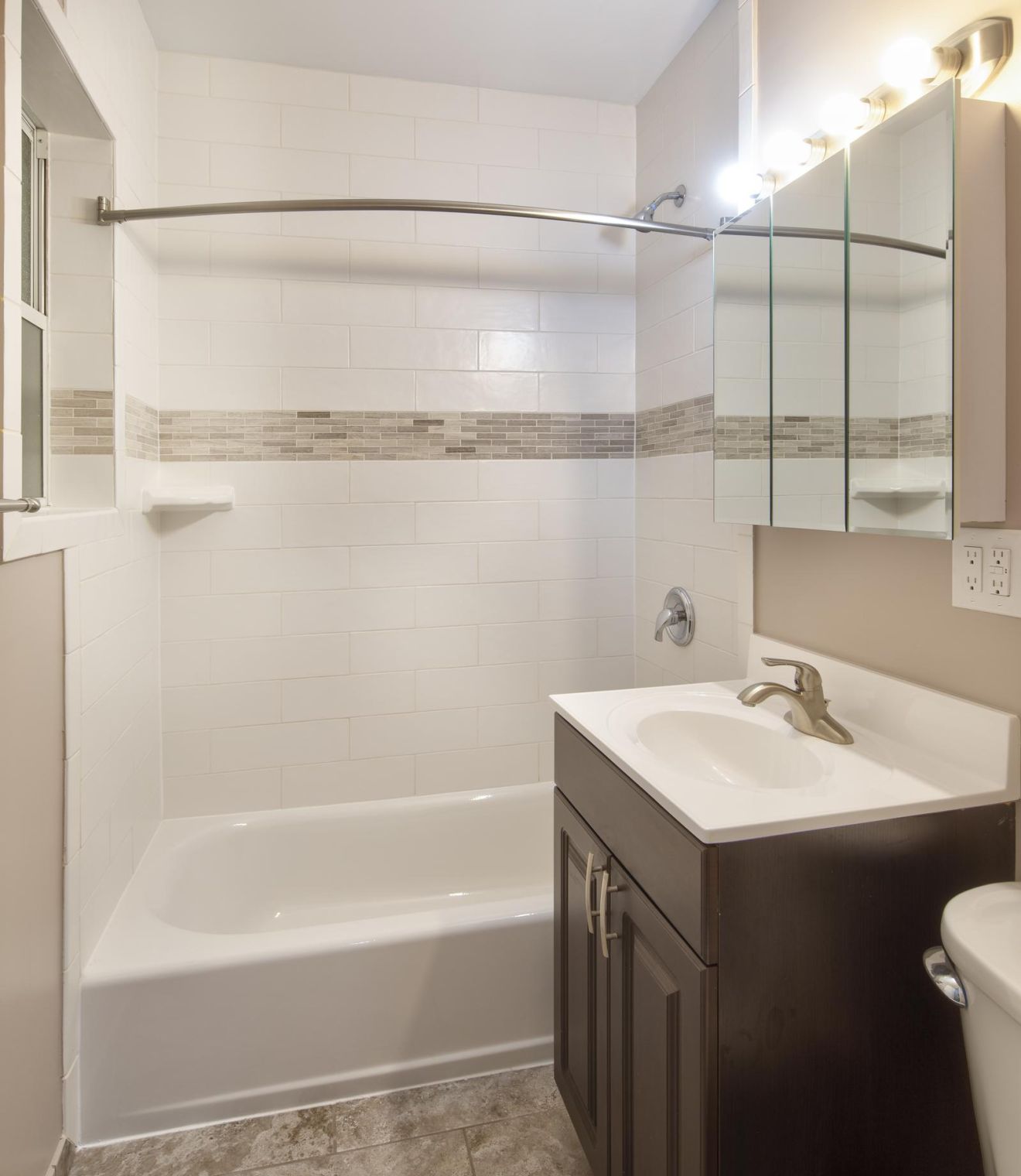 Modern bathroom with a white tub, dark vanity, mirror cabinet, and tiled walls with accent strip.