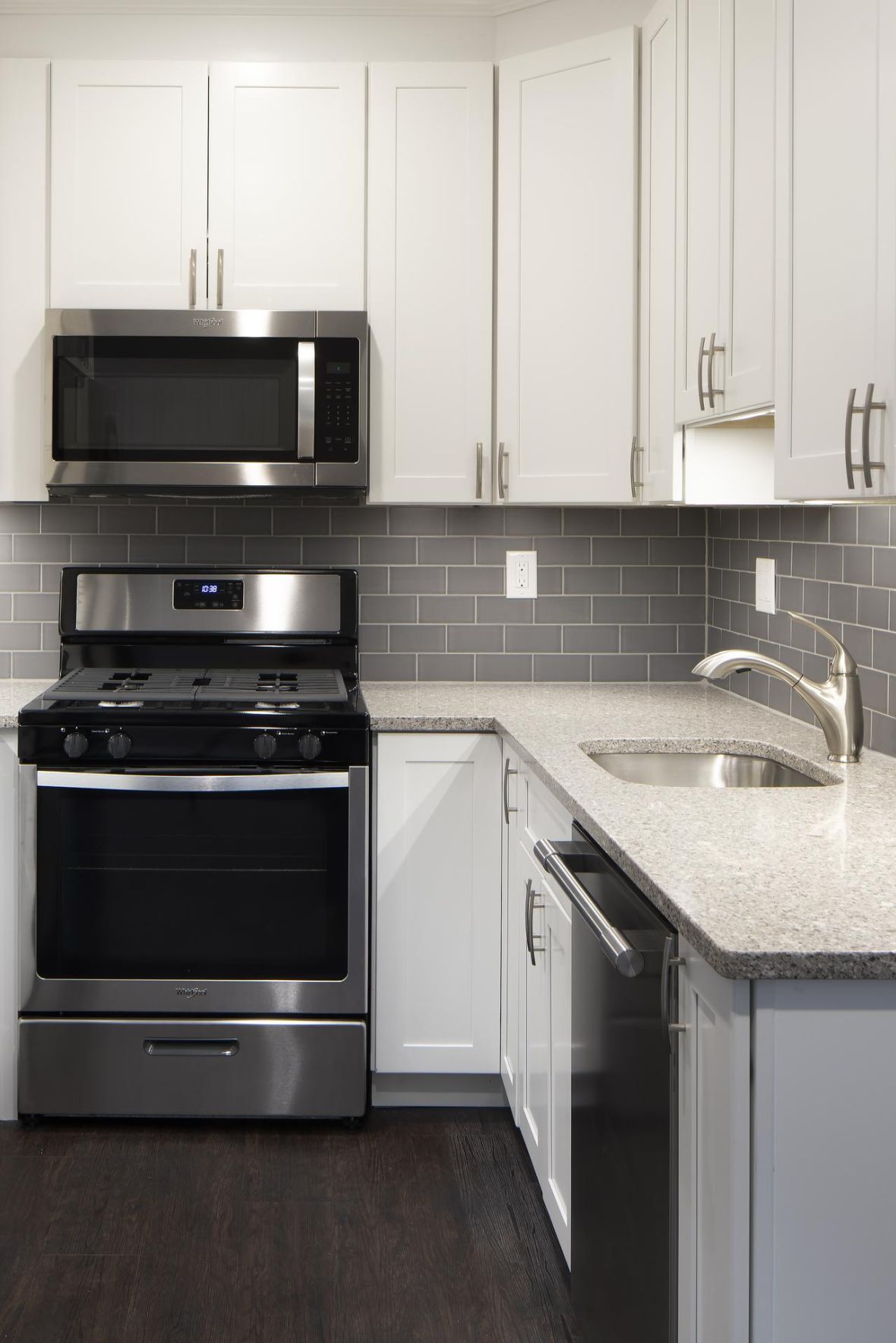 Modern kitchen with stainless steel appliances, gray tile backsplash, and white cabinets.