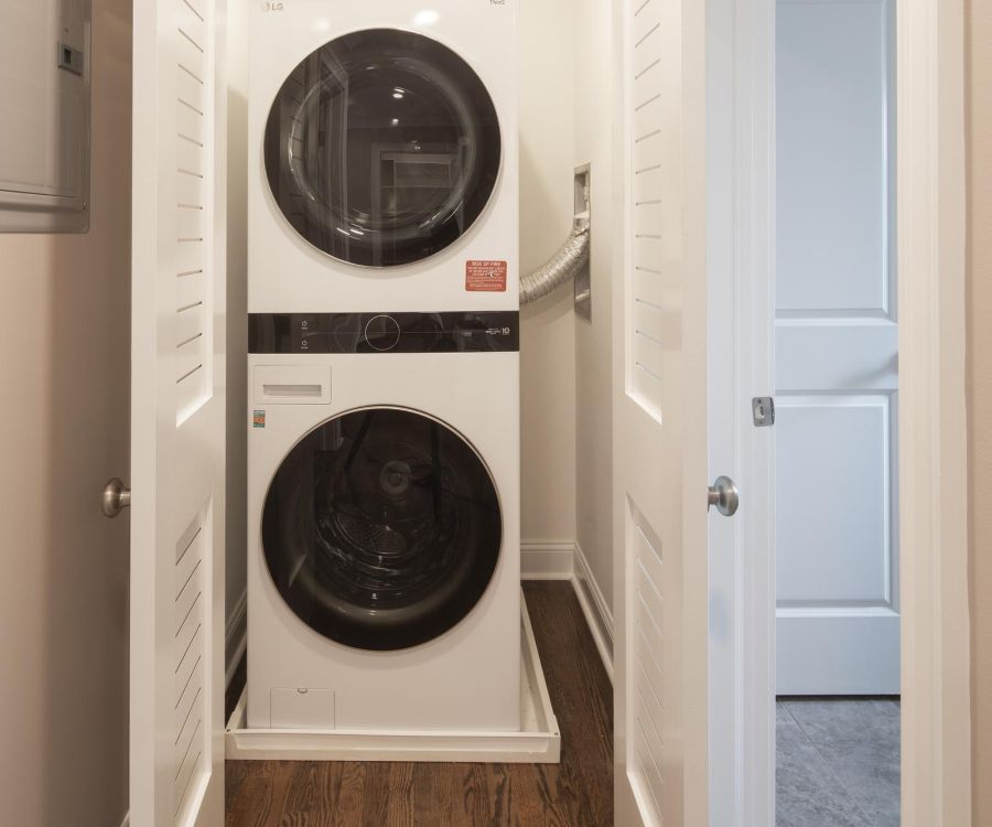 Stacked washer and dryer in a small laundry closet with white bi-fold doors and wood flooring.