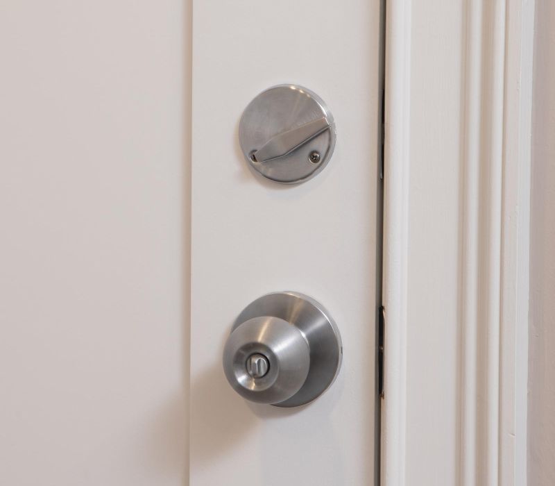 Close-up of a white door with a silver deadbolt lock and a round doorknob featuring a keyhole.