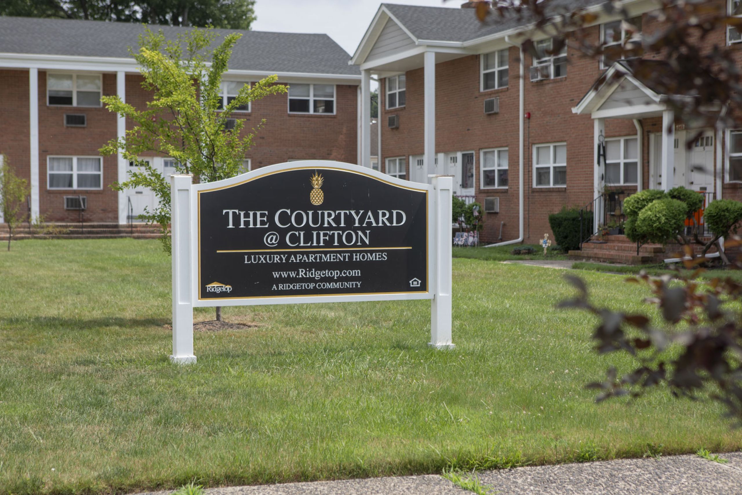 The Courtyard @ Clifton A sign for The Courtyard @ Clifton luxury apartment homes stands on a grassy lawn in front of brick buildings.