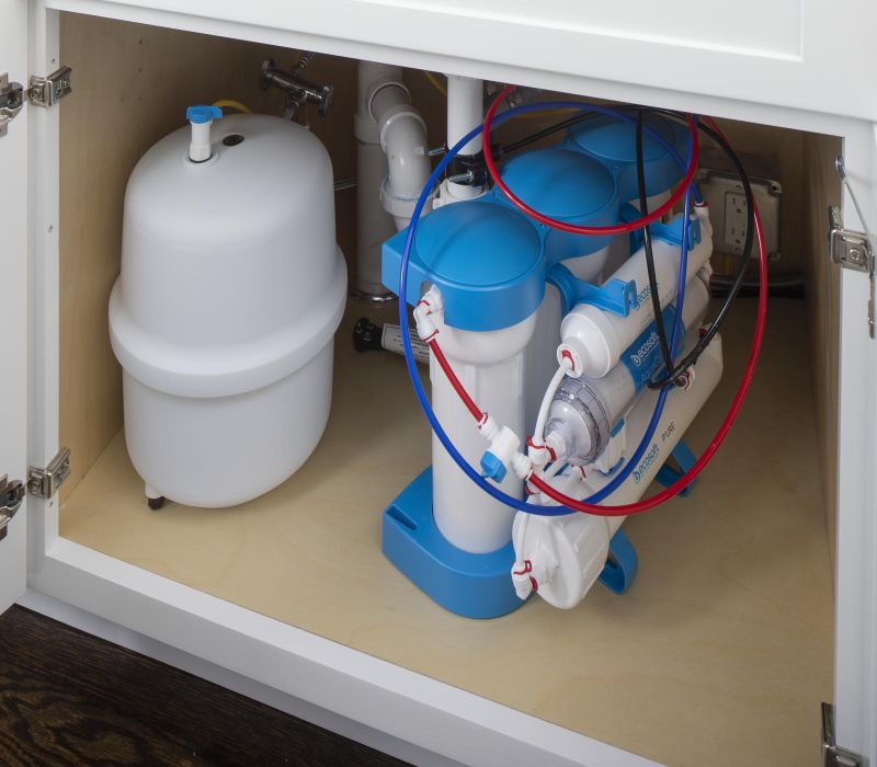 Under-sink reverse osmosis water filtration system with blue and white canisters and connected tubes.