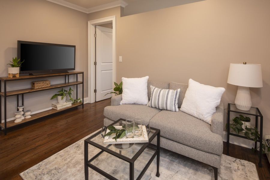 The Courtyard @ Clifton A cozy living room with a gray sofa, TV, plants, and a tray on a glass coffee table.
