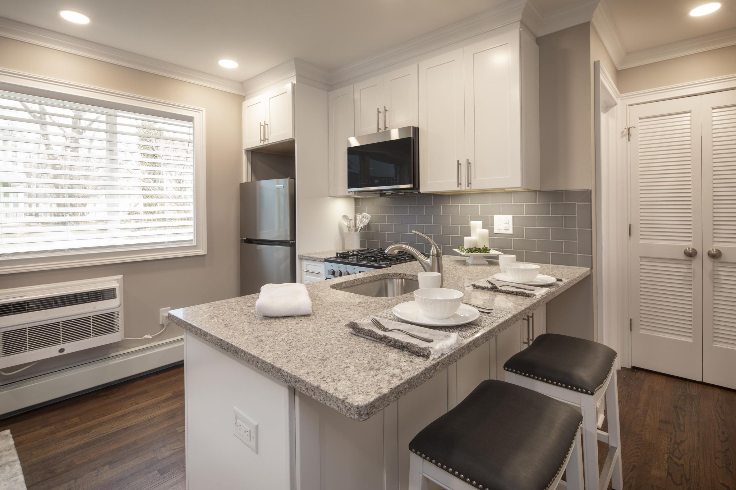 The Courtyard @ Clifton Modern kitchen with white cabinets, gray countertops, and a breakfast bar set with dishes and stools.