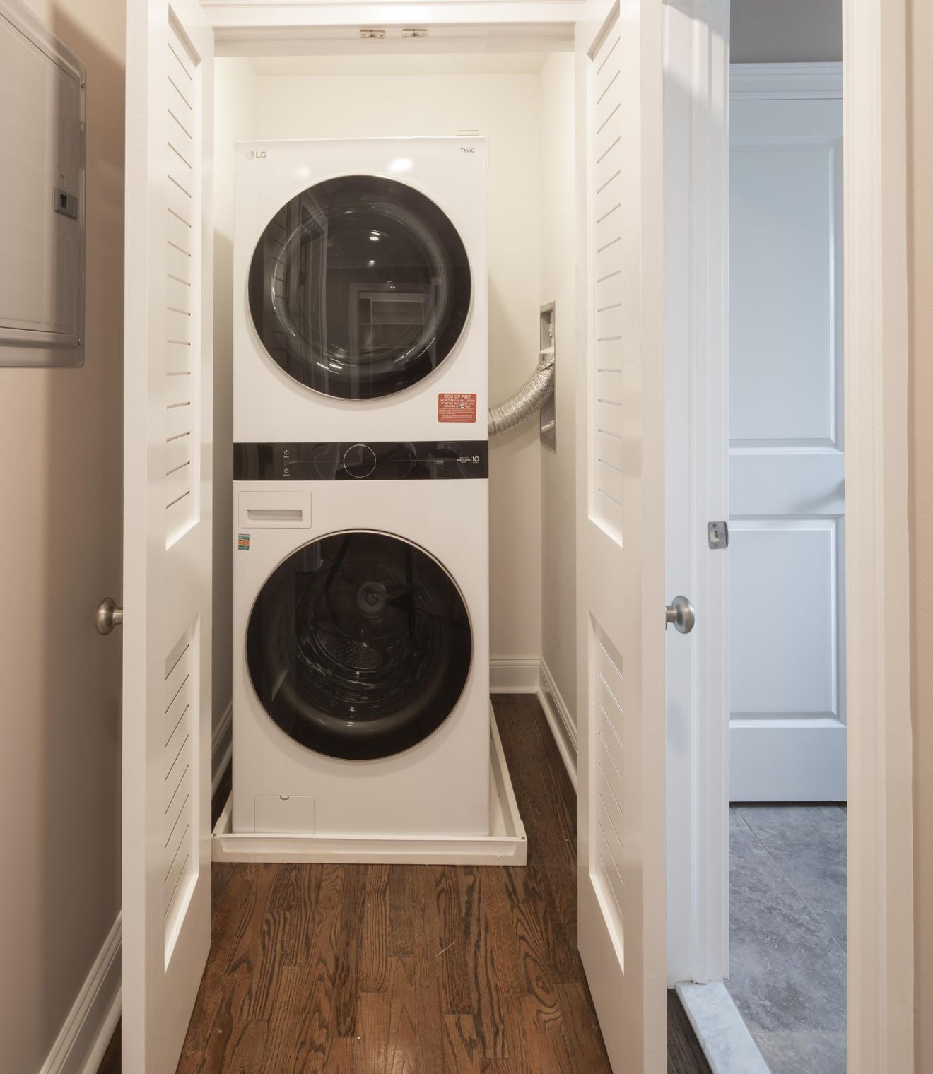 Stacked washer and dryer in a small laundry closet with white bi-fold doors and wood flooring.