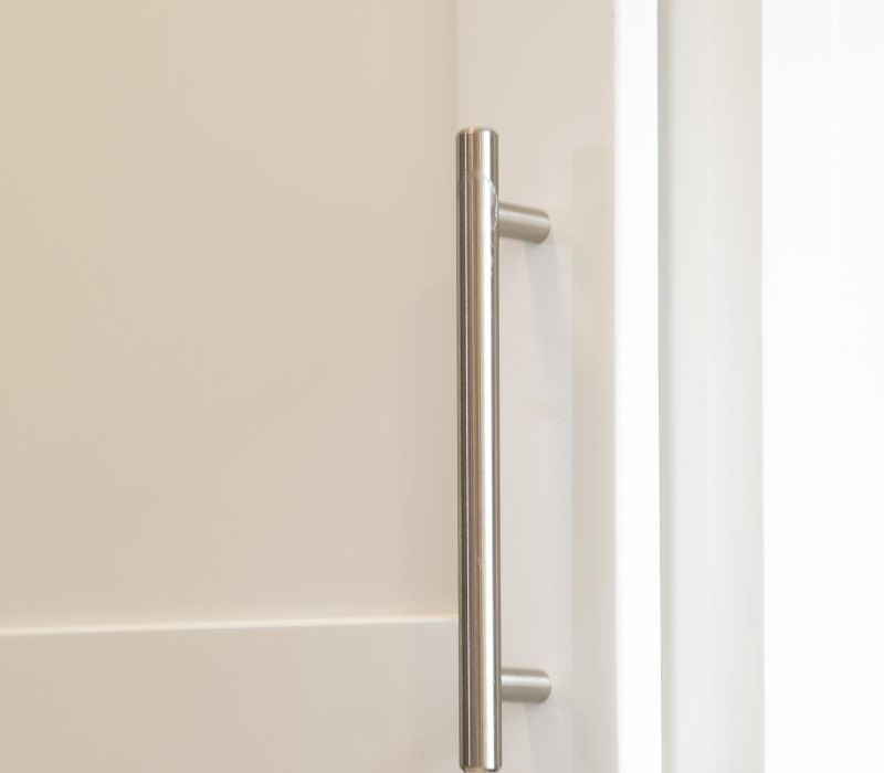 Close-up of a white cabinet door with a vertical brushed metal handle.