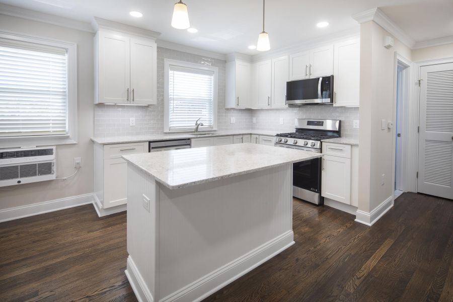 The Courtyard @ Clifton Modern white kitchen with island, stainless steel appliances, and hardwood floors.