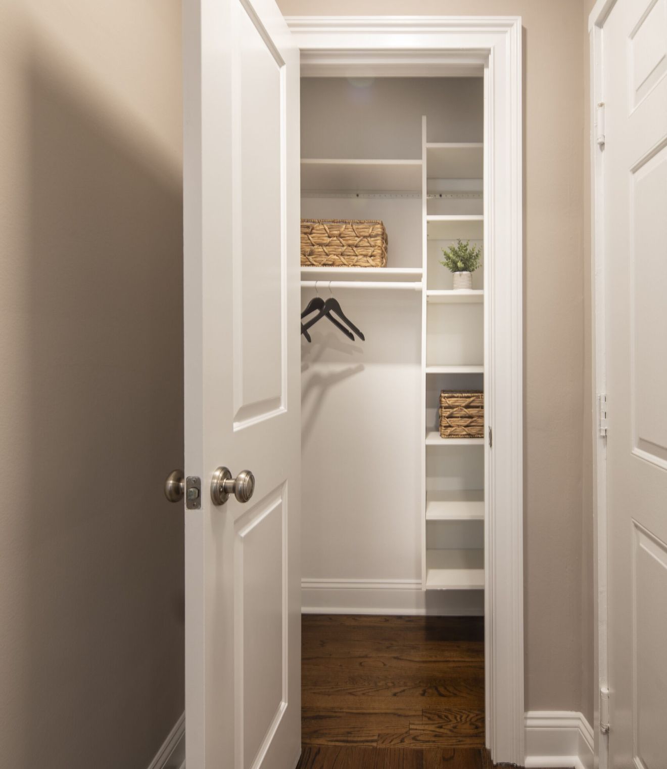 East Hill closet with white shelves, a few baskets, some black hangers, and a potted plant on wooden floor.