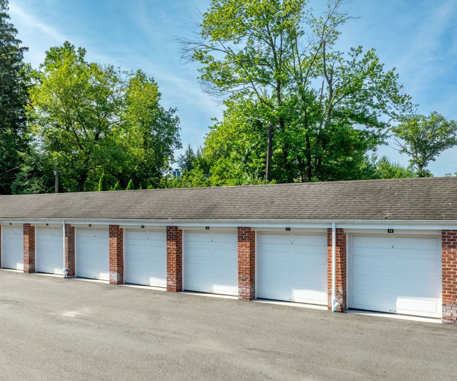 The East Hill Row of brick garages with white doors and trees in the background under a clear blue sky.