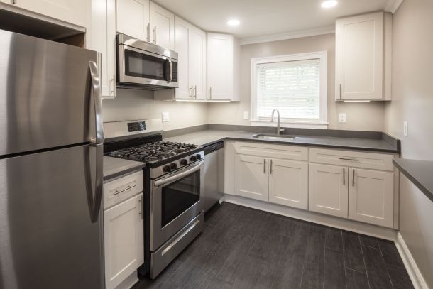 The East Hill Modern kitchen with stainless steel appliances, white cabinets, gray countertops, and dark wood flooring.