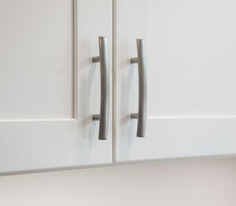 East Hill Close-up of two silver handles on white cabinet doors.