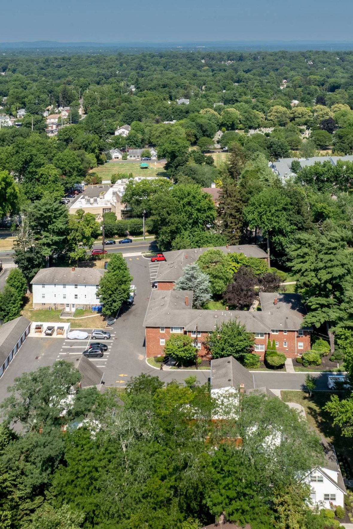 The East Hill Empty outdoor tennis court with nets, surrounded by trees and buildings, under a partly cloudy sky.