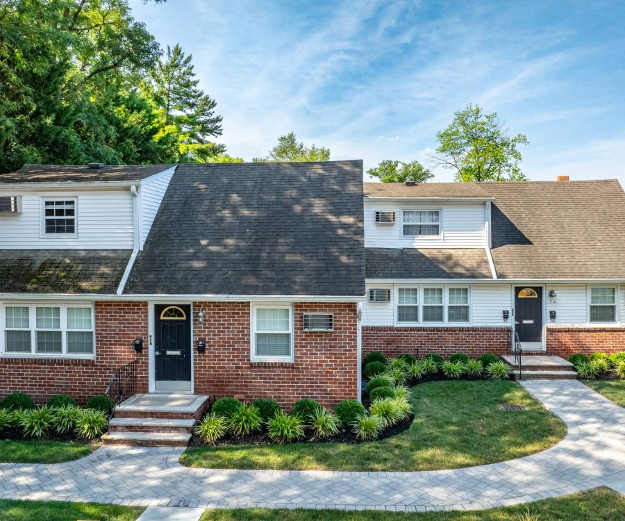The East Hill Red-brick duplex with white trim, black doors, and landscaped walkway on a sunny day.