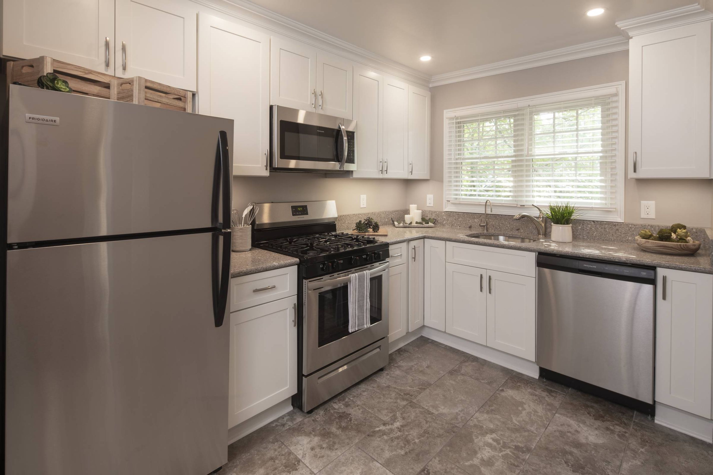 East Hill Modern kitchen with white cabinets, stainless steel appliances, granite countertops, and a window above the sink.