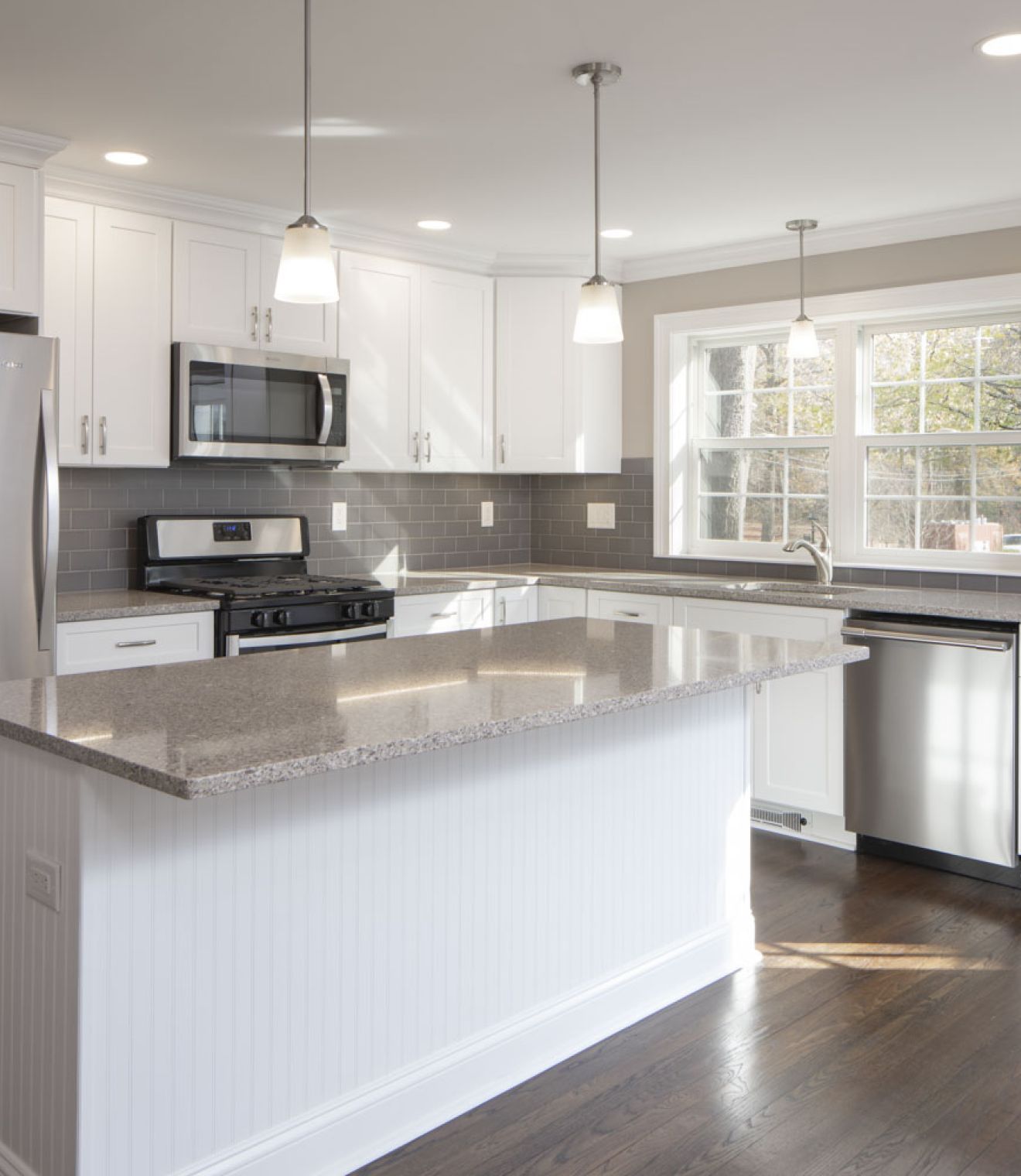 The East Hill Modern kitchen with white cabinets, stainless steel appliances, and a large island under pendant lights.
