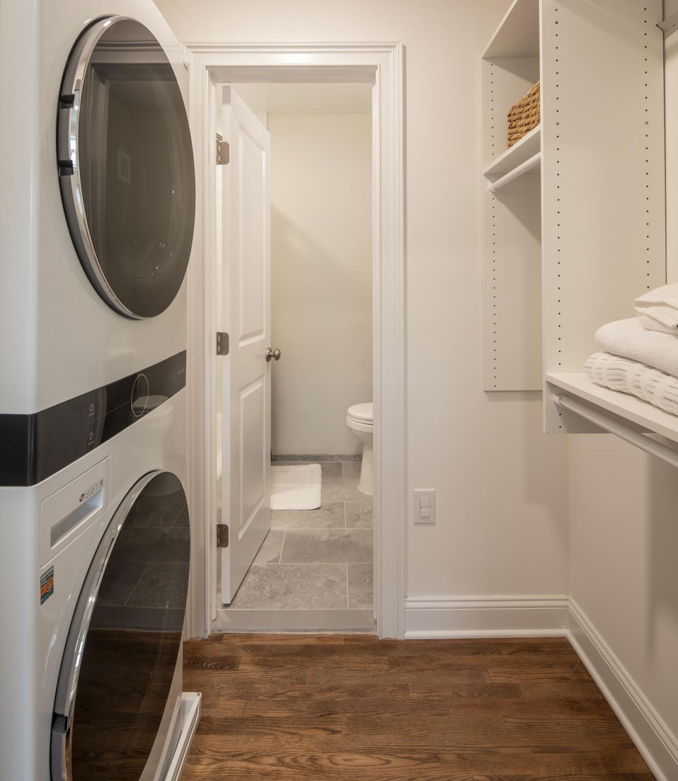 Stacked washer and dryer in a laundry room with a view into a bathroom through an open door.