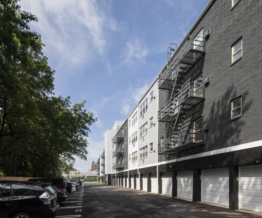 Four-story apartment building with black and white exterior, garages below, and parking lot with cars.