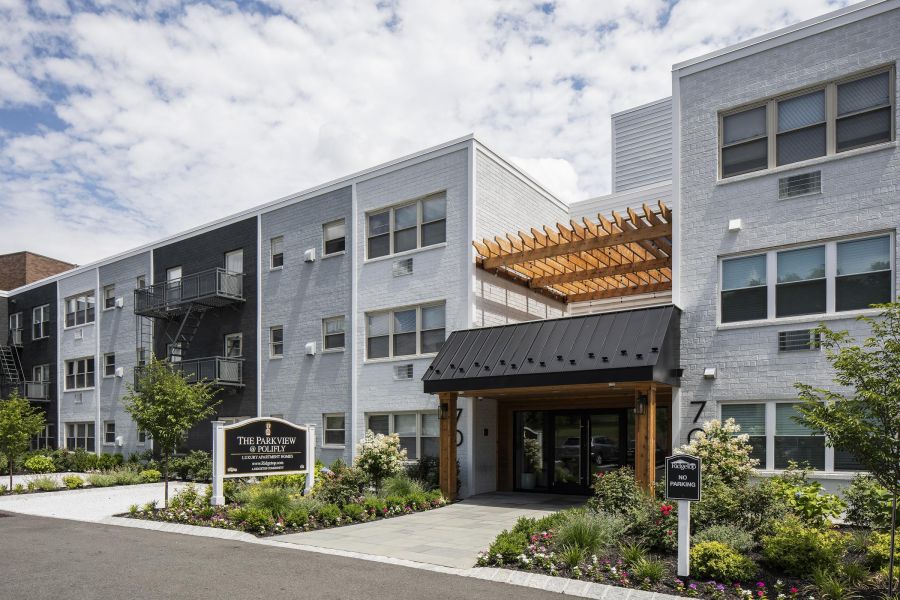 The Parkview @ Polifly A modern apartment building with landscaped gardens and a wooden entrance canopy under a partly cloudy sky.