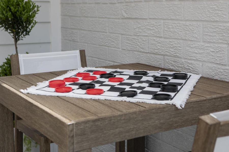The Parkview @ Polifly Checkers game in progress on a wooden table outdoors, with red and black pieces on a fabric board.
