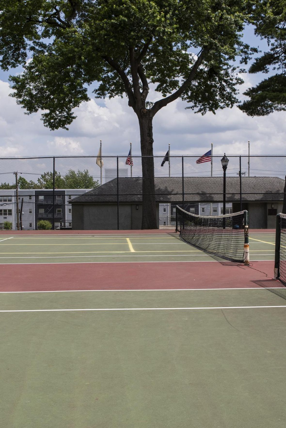The Parkview @ Polifly Empty outdoor tennis court with nets, surrounded by trees and buildings, under a partly cloudy sky.