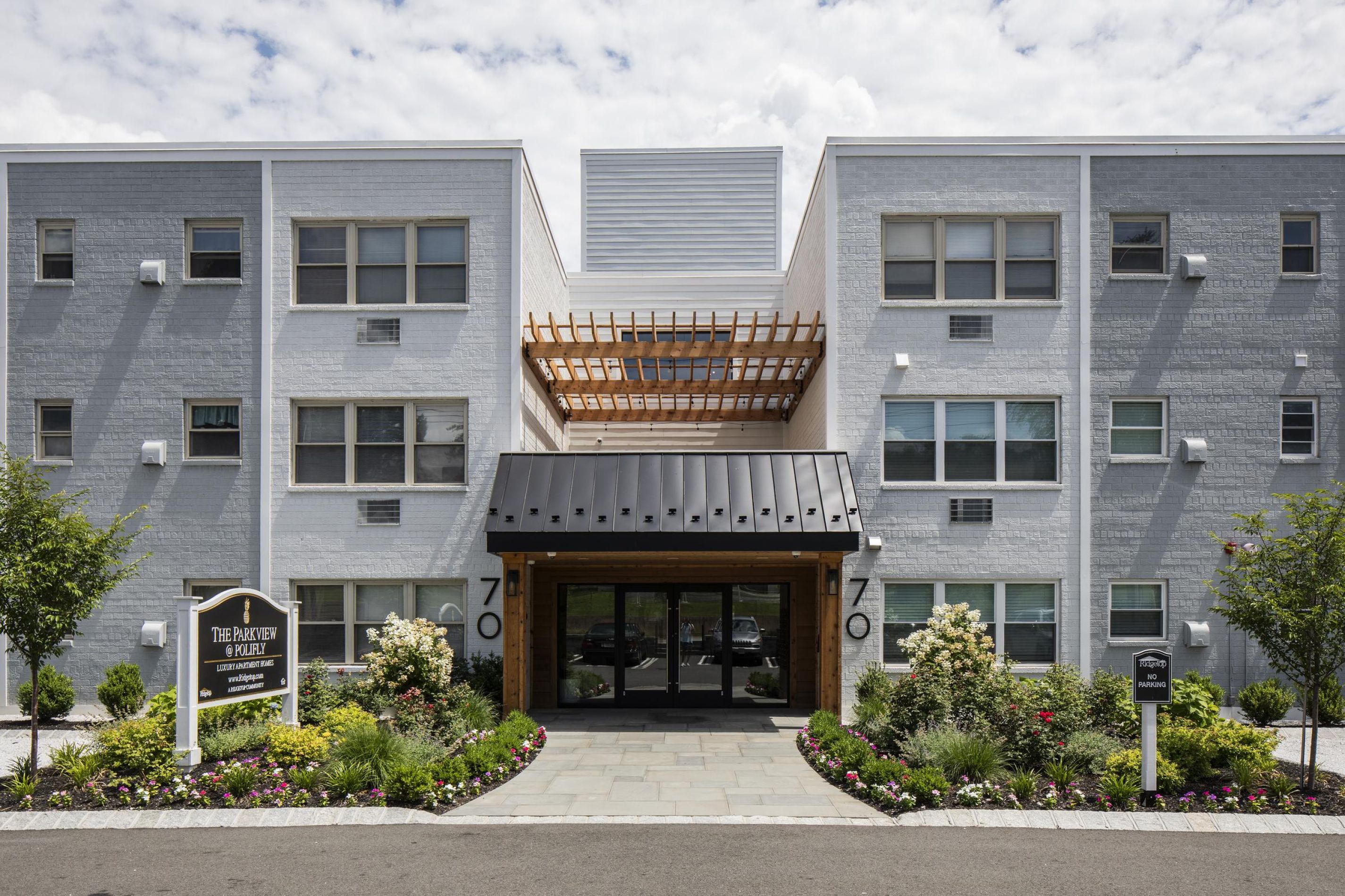 Modern three-story apartment building with a landscaped entrance and a wooden pergola over the doorway.