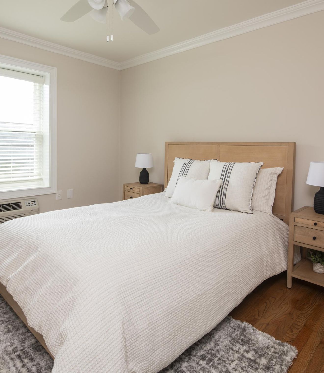 A bright bedroom with a neatly made bed, two bedside tables, lamps, and a window letting in natural light.
