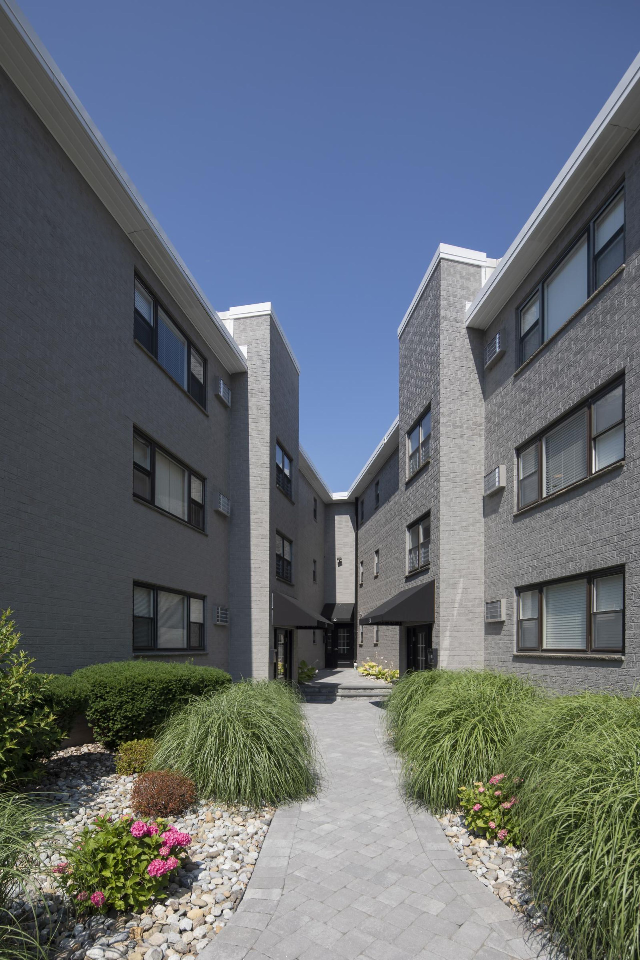 Villa Malta A modern apartment building with landscaped gardens and a wooden entrance canopy under a partly cloudy sky.