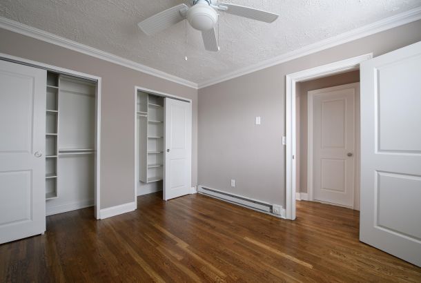 Villa Malta Empty bedroom with hardwood floor, open closets, white doors, and a ceiling fan.