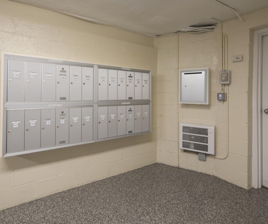 Villa Malta Wall-mounted mailboxes in a building hallway next to a door and an intercom on a beige wall.