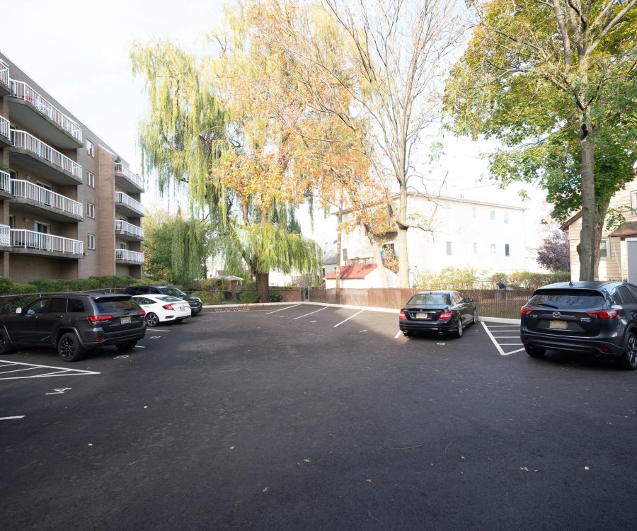 An apartment building parking lot with several parked cars and trees with autumn leaves.