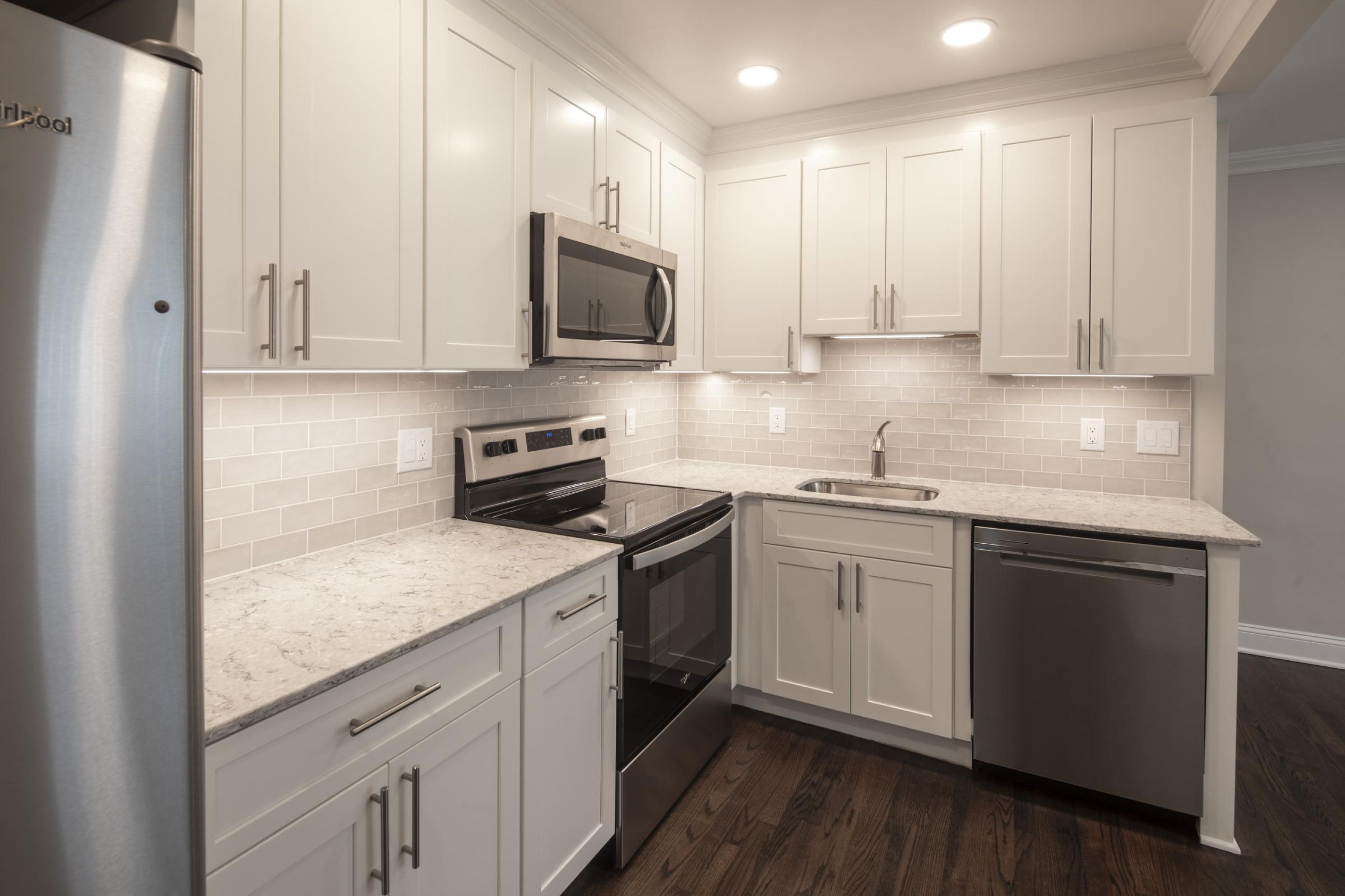 Villa Malta Modern kitchen with white cabinets, stainless steel appliances, tile backsplash, and dark wood flooring.
