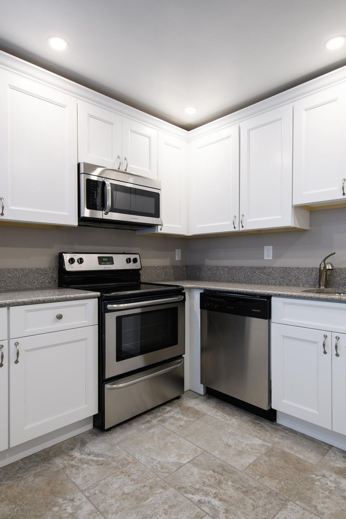 Villa Malta Modern kitchen with white cabinets, stainless steel appliances, and granite countertops under bright lighting.