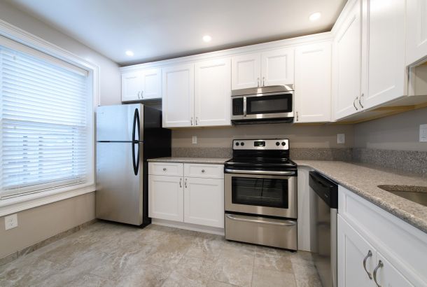 Villa Malta Modern kitchen with white cabinets, stainless steel appliances, and a large window with blinds.