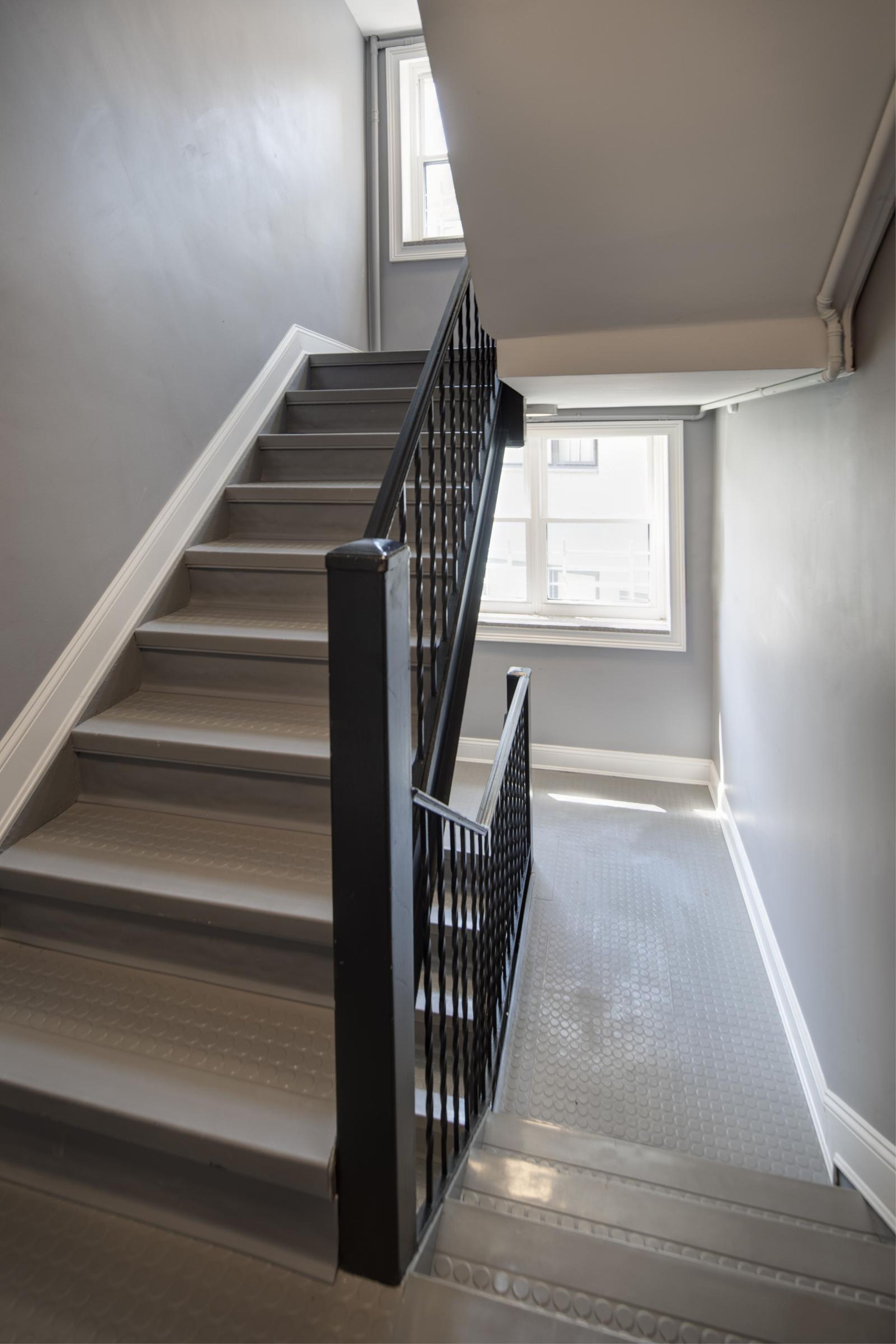 Villa Malta Two gray armchairs with pillows sit by a small table in a modern, gray-toned hallway near an elevator.