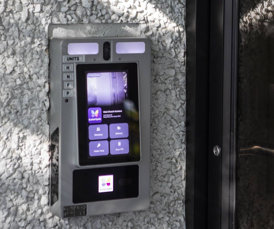 A touchscreen intercom system mounted on a textured wall next to a glass door.