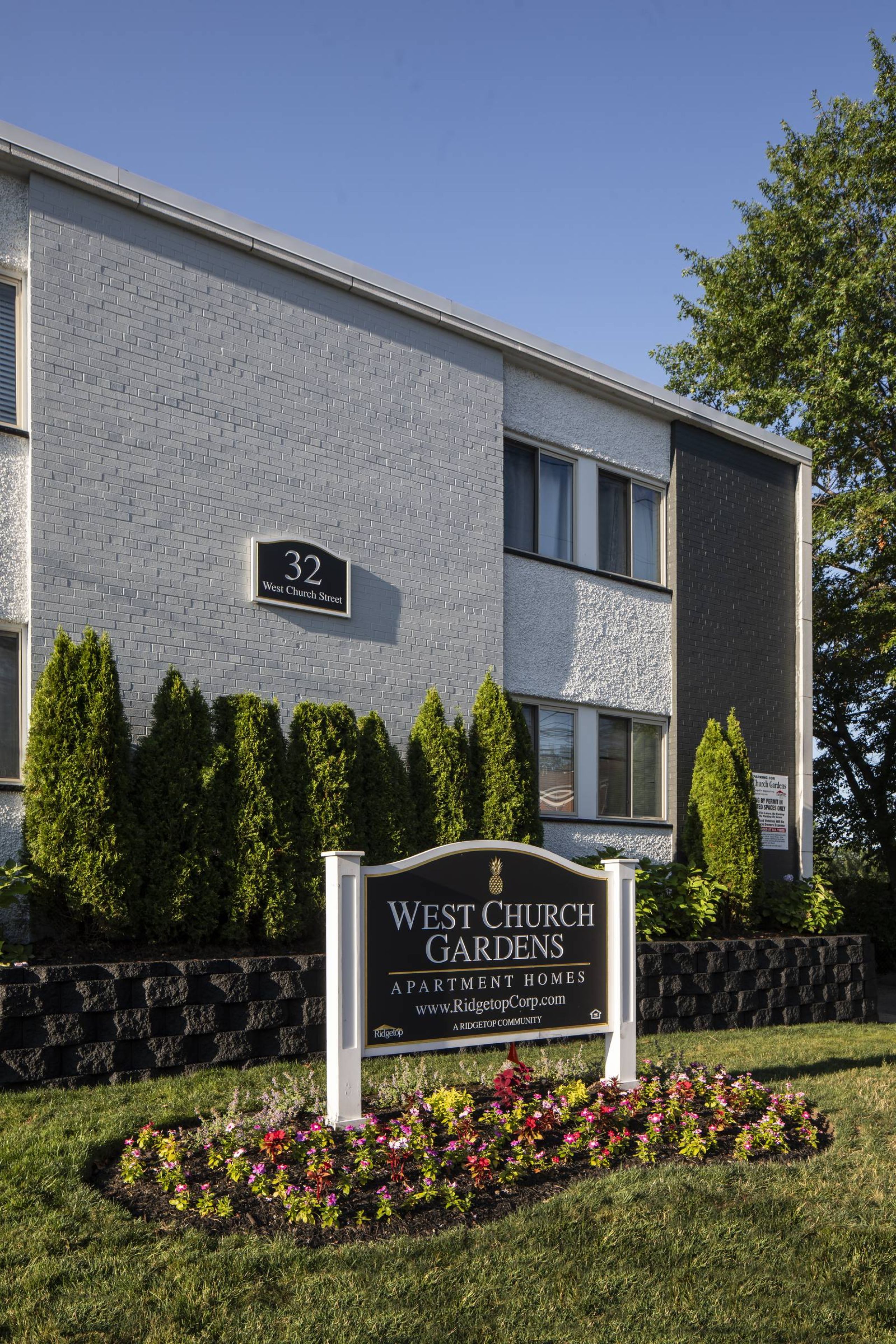 West Church Gardens A modern apartment building with landscaped gardens and a wooden entrance canopy under a partly cloudy sky.