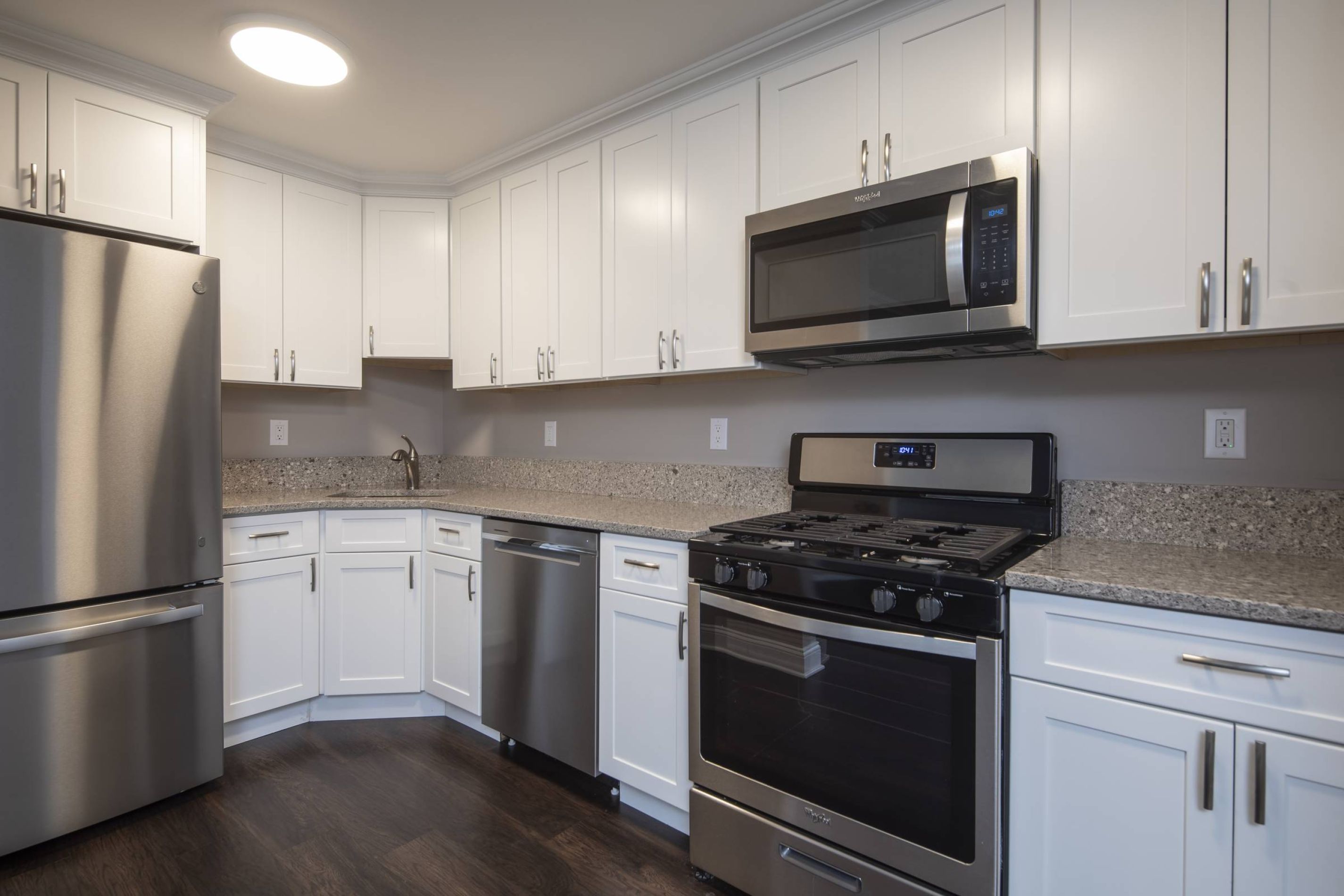 Modern kitchen with white cabinets, stainless steel appliances, granite countertops, and dark wood flooring.