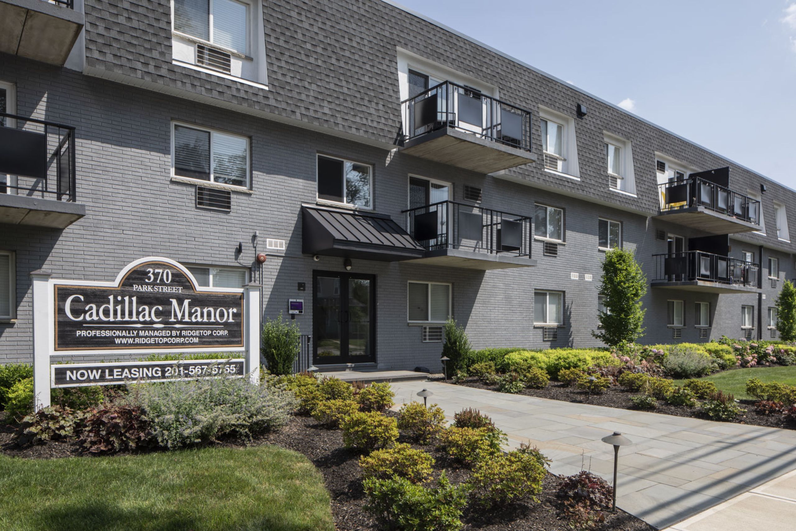 West Church GardensPatio with wooden pergola, outdoor seating, chairs, and plants, overlooking a green lawn with flags.