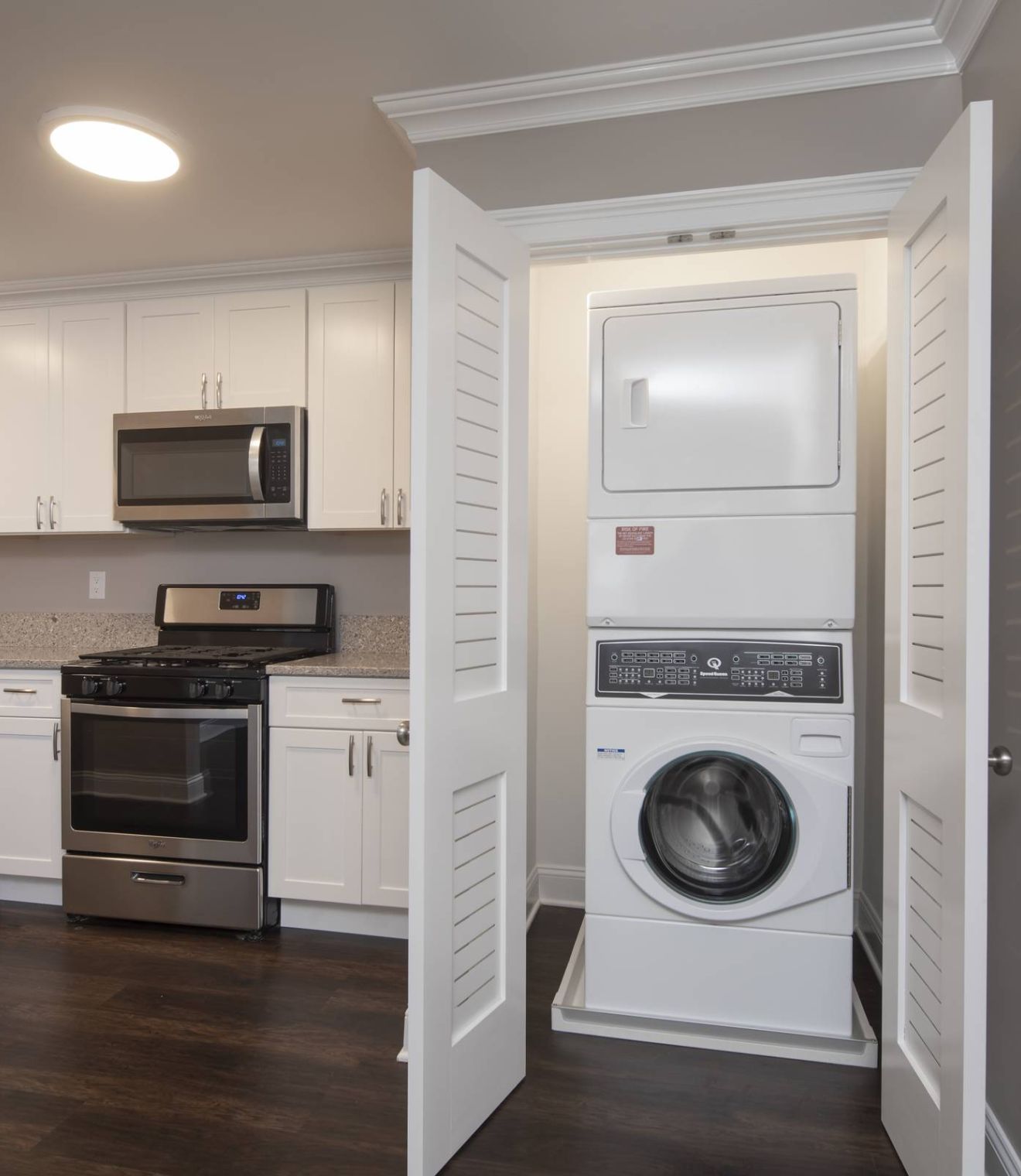 Stacked washer and dryer in a laundry room with a view into a bathroom through an open door.