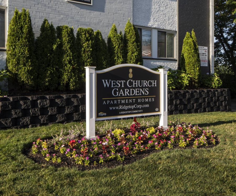 Patio with wooden pergola, outdoor seating, chairs, and plants, overlooking a green lawn with flags.