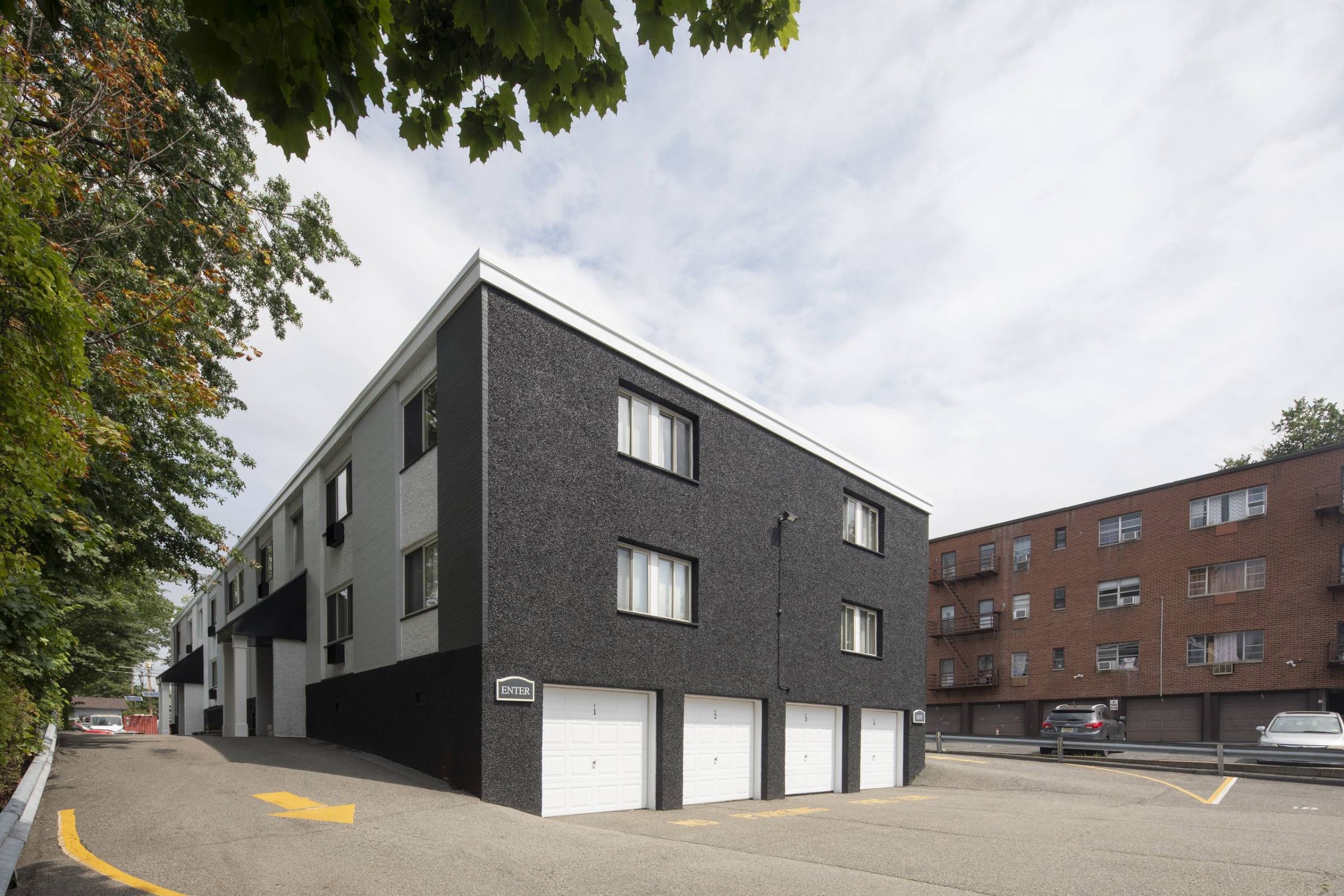 West Church Gardens Two gray armchairs with pillows sit by a small table in a modern, gray-toned hallway near an elevator.