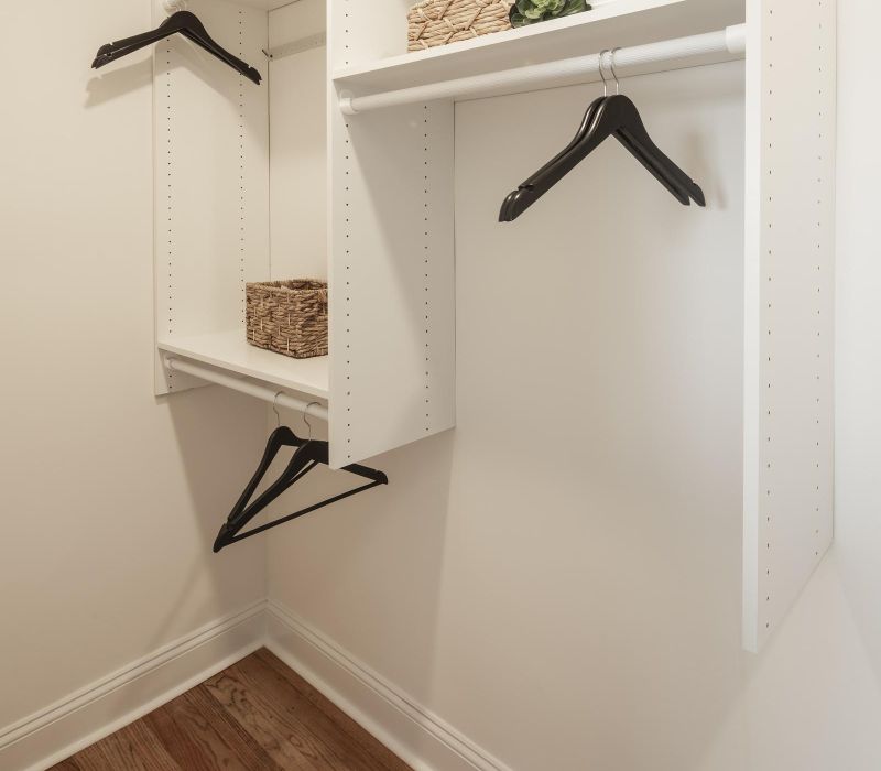 Minimalist walk-in closet with white shelves, black hangers, wicker baskets, and wooden floor.