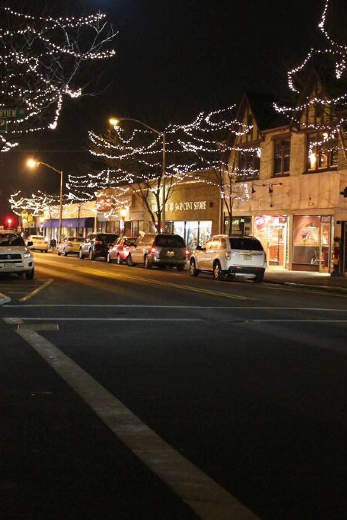 Westwood Manor Empty outdoor tennis court with nets, surrounded by trees and buildings, under a partly cloudy sky.