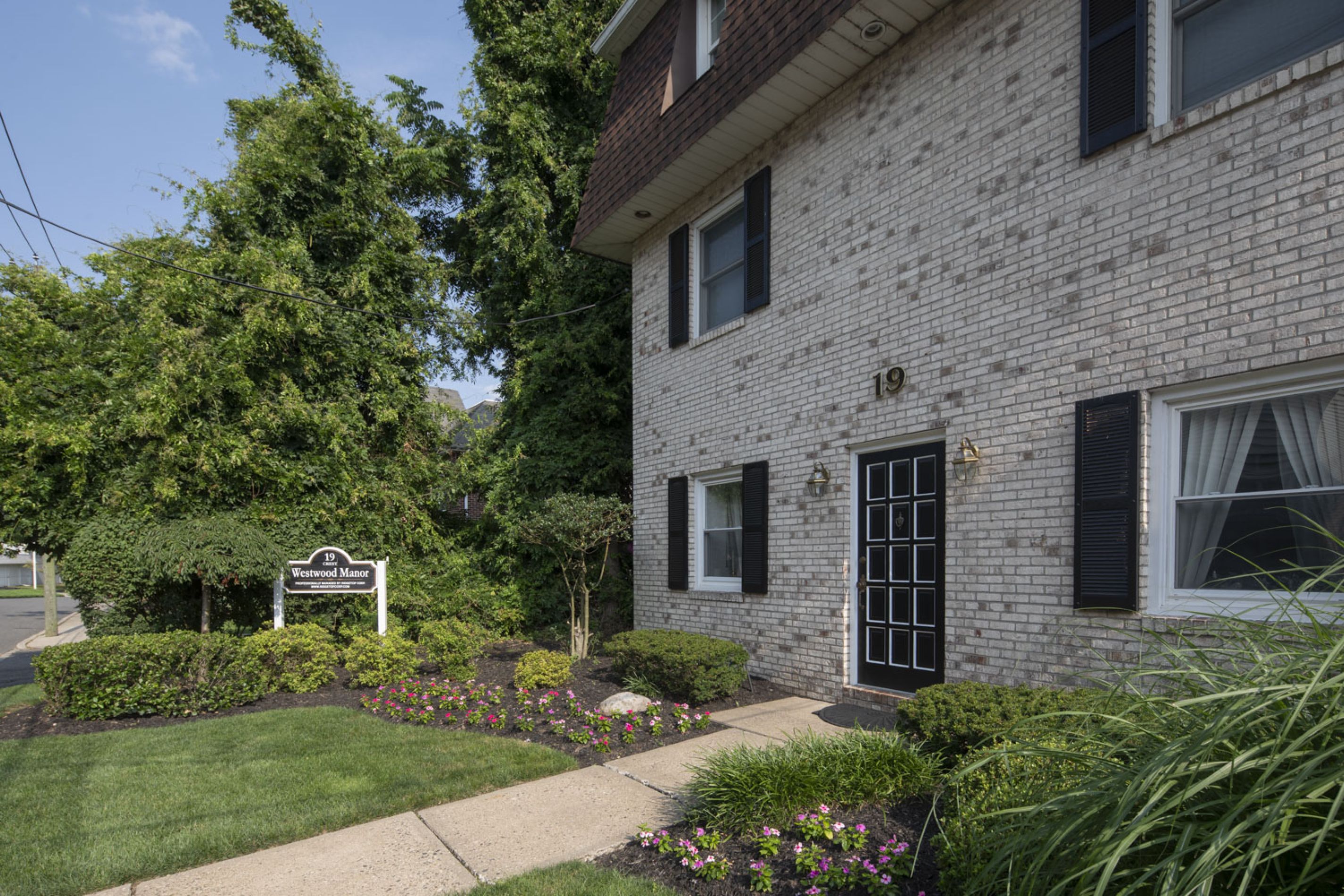 A brick apartment building with black shutters, a black door, and landscaped garden in front.