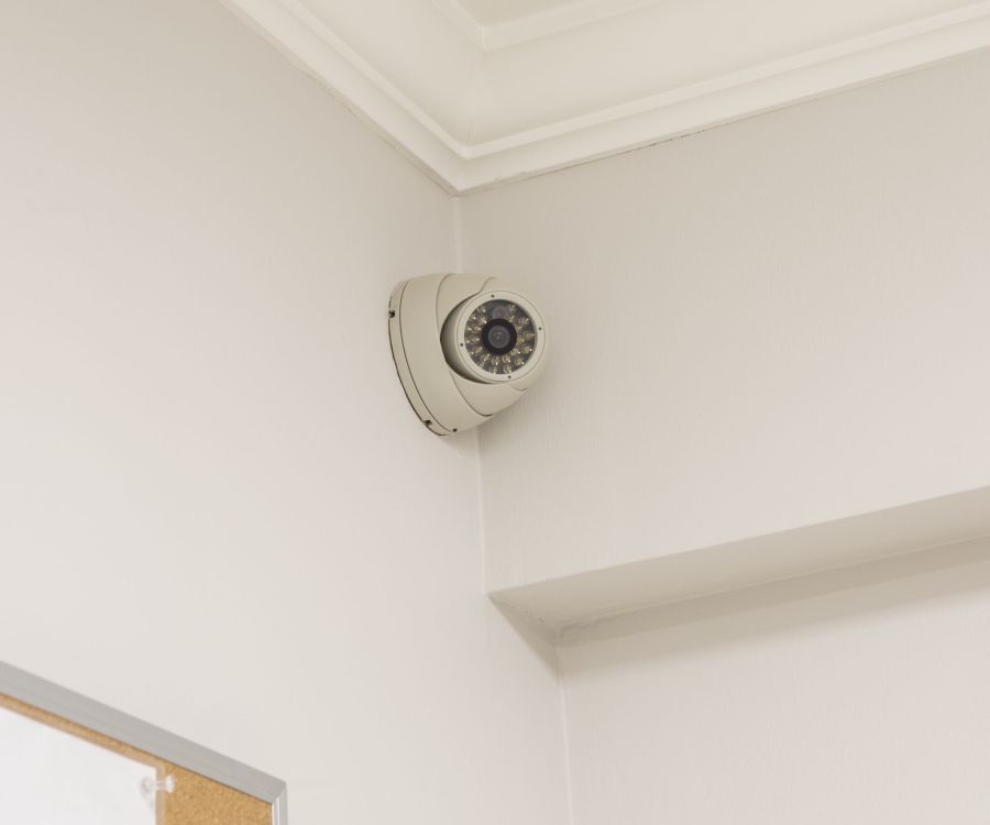 A security camera mounted on the corner of a white ceiling.